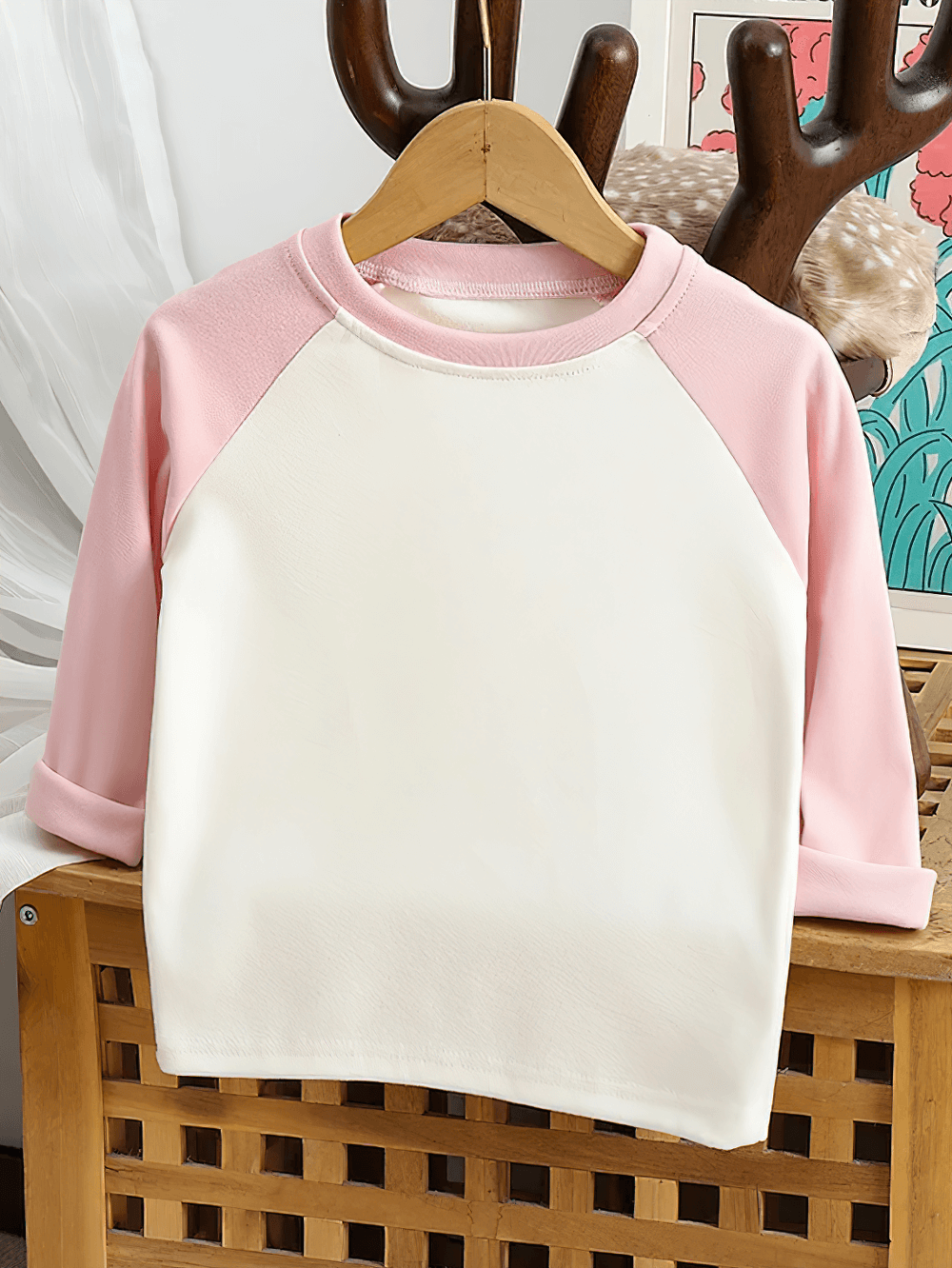 Adorable kids' raglan sleeves top with round neck in pink and white, hanging on a wooden hanger.